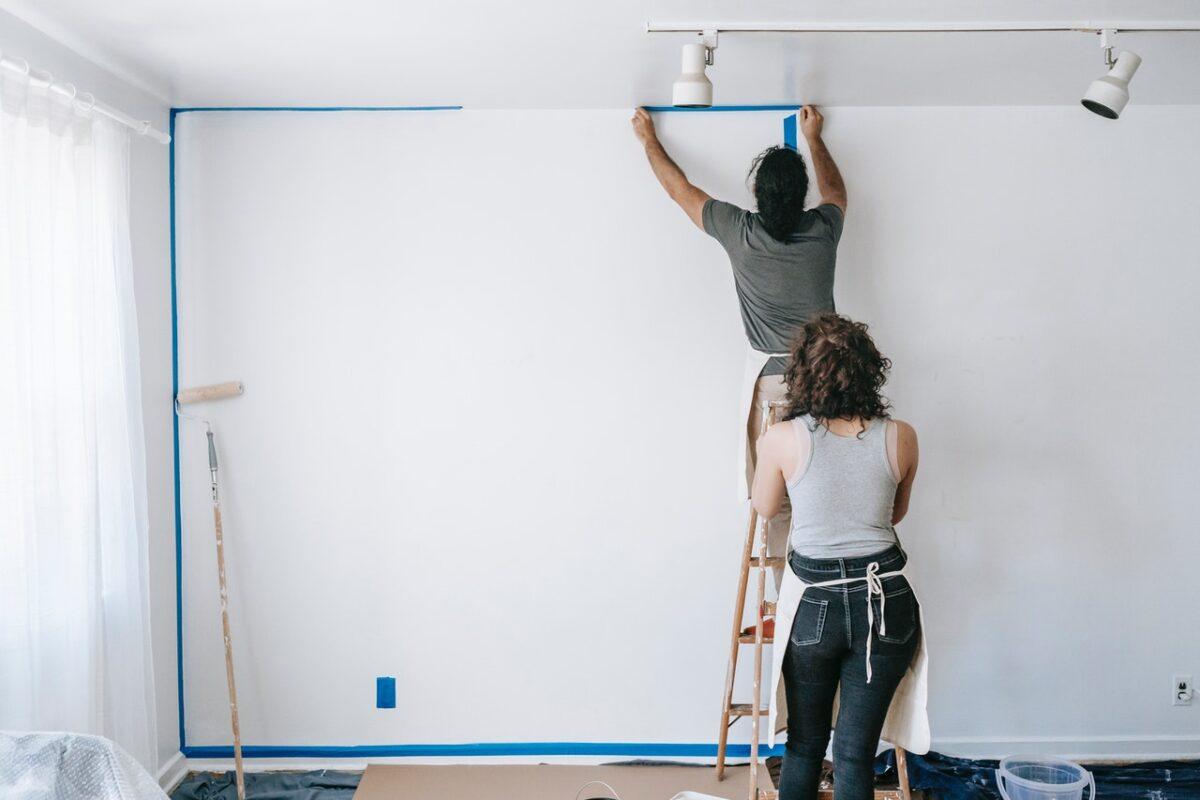 casal passando fita adesiva na parede para fazer a pintura da casa