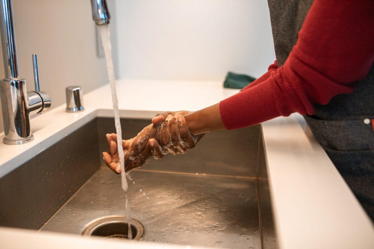torneira de pia ligada com as mãos de uma pessoa sendo lavada