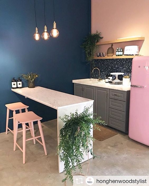Cozinha compacta rosa, com parede azul e chão cinza queimado.