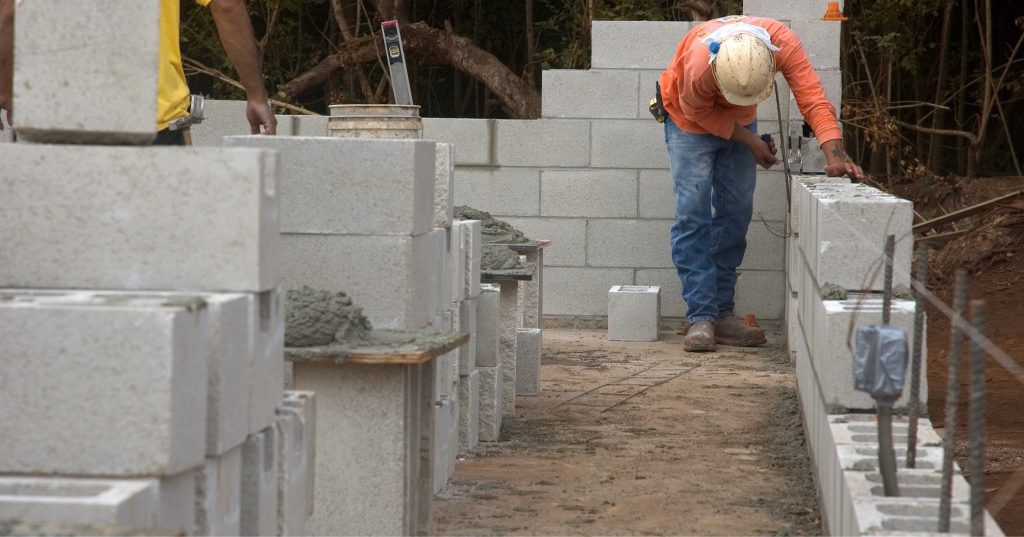 Um mestre de obras trabahando na alvenaria, montando blocos de concreto.