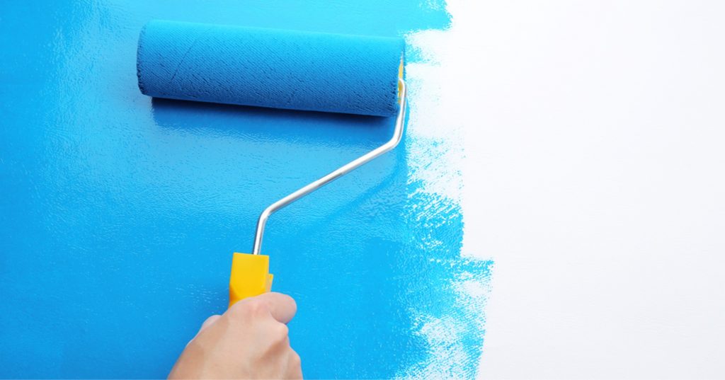 Uma mão segurando um rolo de pintura enquanto pinta uma parede com tinta azul.